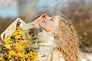 Portrait of a young woman with blond hair holding a bouquet of mimosa in her hands. Spring