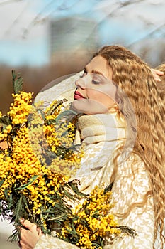 Portrait of a young woman with blond hair holding a bouquet of mimosa in her hands. Spring