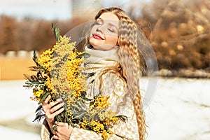 Portrait of a young woman with blond hair holding a bouquet of mimosa in her hands. Spring