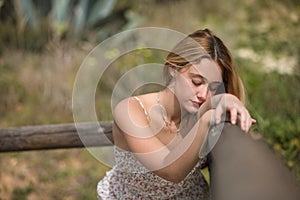 Portrait of young woman, blonde and beautiful, with a suit of flowers, with closed eyes leaning on a railing, sad and melancholic