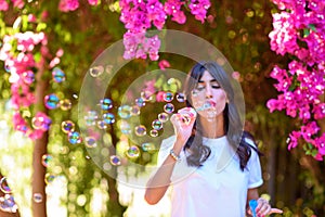 Happy beautiful young woman blowing soap bubbles outdoor.