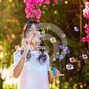 Portrait of Young woman blowing soap bubbles on pink flowers background on the beach.