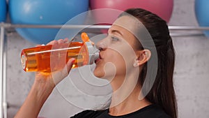 Portrait young woman breathing and drinking water from fitness bottle in gym. Tired woman relaxing and drinking water