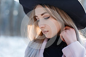 Portrait of a young woman with brown eyes with lips with blond hair with beautiful make-up in an elegant black hat