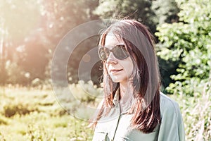 portrait of young woman with brown hair wearing sunglasses. Girl in nature enjoying sunny summer day