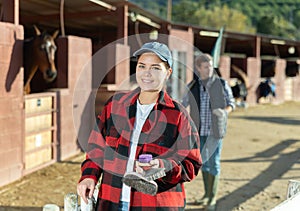 Portrait of young woman with brushes in her hands for cleaning and caring for horses at horse farm