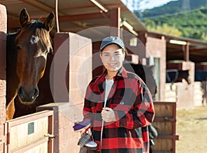 Portrait of young woman with brushes in her hands for cleaning and caring for horses at horse farm