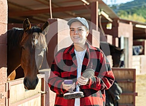 Portrait of young woman with brushes in her hands for cleaning and caring for horses at horse farm