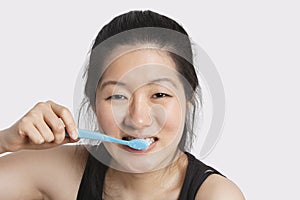 Portrait of a young woman brushing her teeth over light gray background