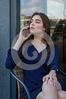 Portrait of a young woman in a cafe on the street sitting at a table and talking on the phone. Lifestyle beauty woman