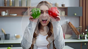 Portrait of young woman changing emotions with colorful peppers at home kitchen.