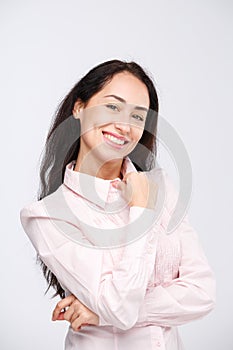 Portrait of a young woman with a charming toothy smile, black hair and brown eyes on a white background in a pink shirt. Positive