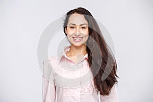 Portrait of a young woman with a charming toothy smile, black hair and brown eyes on a white background in a pink shirt. Positive