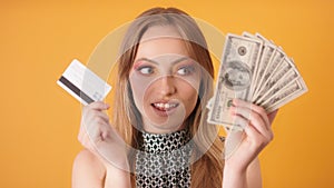 Portrait of a young woman choosing cash over the credit card. Close up shot isolated on the orange background