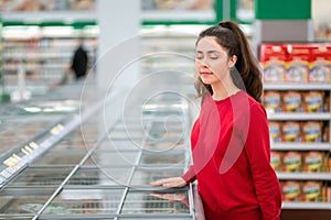 Portrait of a young woman choosing frozen food, near the refrigerators. The concept of grocery shopping