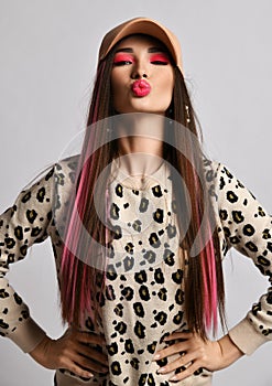 Portrait of young woman with colored straight hair in leopard pattern print pullover sweater and beige cap sending kiss