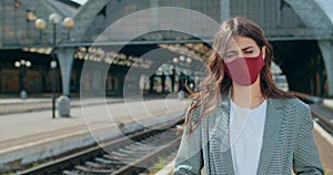 Portrait of young woman in cotton facial mask standing at railway station. Crop view of serious millennial girl looking