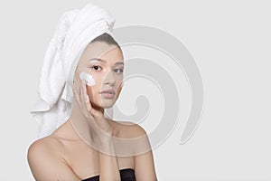 Portrait of a young woman with cream on her face. hand touch to the cheek. A towel on her head