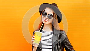 portrait young woman with cup of juice wearing a black round hat, sunglasses over orange background