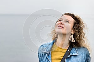 Portrait of a young woman with curly hair looking up dreaming, outdoors, sweet.