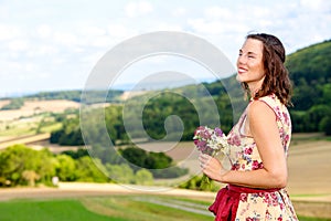 Young woman in dirndl standing in meadow with flowers and enjoying the sun