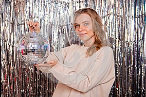 Portrait of a young woman with a disco ball in her hands posing against a shiny background