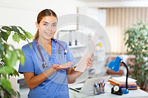 Portrait of a young woman doctor in a office, holding an outpatient patient card in her hands