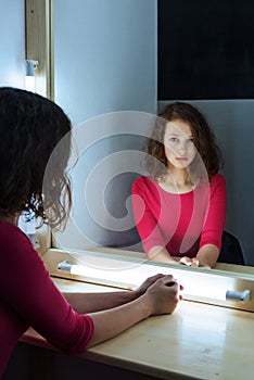 Portrait of a young girl in a dressing room looking closely at the mirror in her reflection
