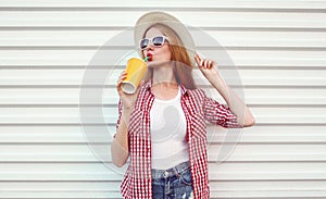 Portrait young woman drinking a juice wearing a summer straw hat, checkered shirt on a white background