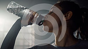 Sportswoman drinking water from sports bottle. Girl holding bottle in hand