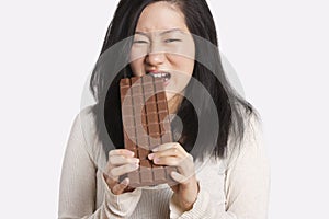 Portrait of a young woman eating a large chocolate bar over light gray background