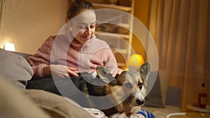 Portrait of young woman embracing her pet. Cute Welsh Corgi puppy resting with owner, spending time together at home