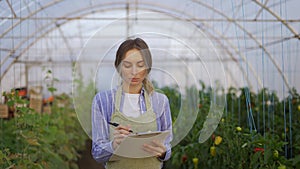 Portrait of young woman farmer in indoor greenhouse, accounting using tablet