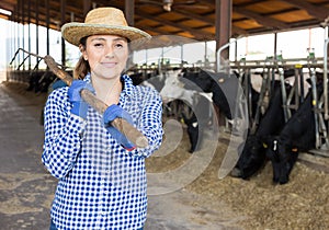 Portrait of a young woman farmer standing in a cowshed, holding a rake