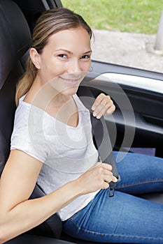 Portrait young woman fastening seatbelt in car