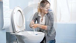 Portrait of young woman feeling disgust and bad smell cleaning toilet at home