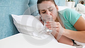 Portrait of young woman feeling unwell lying in bed and dirnking water