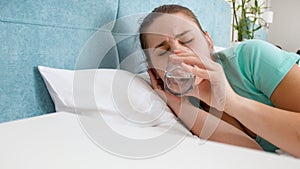 Portrait of young woman feeling unwell lying in bed and drinking water