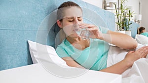 Portrait of young woman feeling unwell lying in bed at home and drinking water