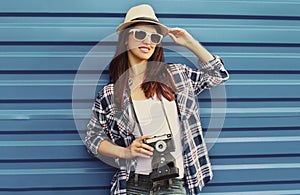 Portrait of young woman with film camera wearing summer straw hat, shirt over a blue background