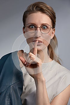 Portrait of young woman with finger on lips, or secret gesture hand sign. Woman making a hushing gesture raising her