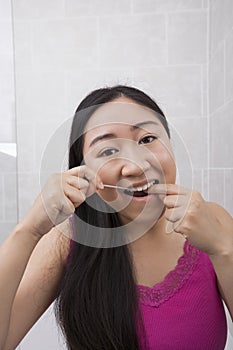 Portrait of young woman flossing her teeth in bathroom