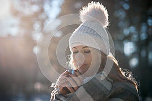 portrait of a young woman in the forest on a sunny winter day with a cup of hot tea