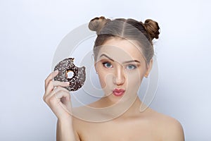 Portrait of a young woman with funny hairstyle and bare shoulders act the ape against white studio background with chocolate donut