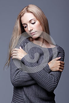 Portrait of young woman in gray woolen sweater with hands crossed. Beautiful girl posing on grey studio background. Female with b