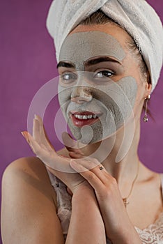 Portrait of young woman with green clay mask on her face isolated on violet