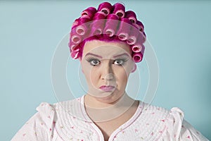 Portrait of young woman grimacing with hair curlers over colored background