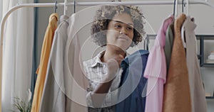 Portrait of young woman hanging clothes on rails touching garments and smiling indoors at home