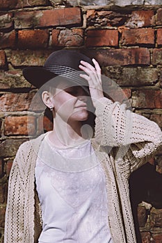 Portrait of a young woman in a hat with closed eyes against a brick wall. Hipster girl outdoors