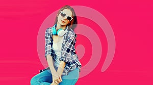 Portrait of young woman with headphones listening to music on pink background